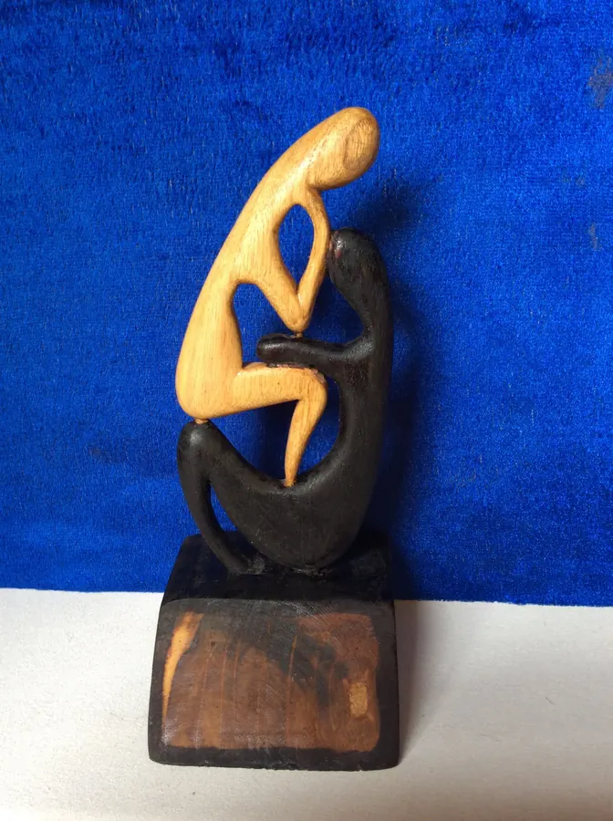 Sculpture en bois : deux figures stylisées, l’une claire, l’autre noire, sur un socle